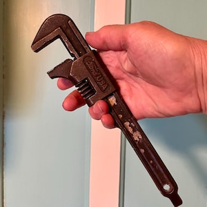 May include: A vintage adjustable wrench, featuring a dark brown finish with signs of wear. The wrench has the text "Ford USA" stamped on the handle. The tool is designed for tightening or loosening nuts and bolts.
