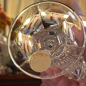 Peut inclure: Un verre en cristal clair et facett&eacute; avec une base ronde et un design g&eacute;om&eacute;trique d&eacute;taill&eacute;. Le verre a un autocollant au fond. Le verre est tenu par une personne.