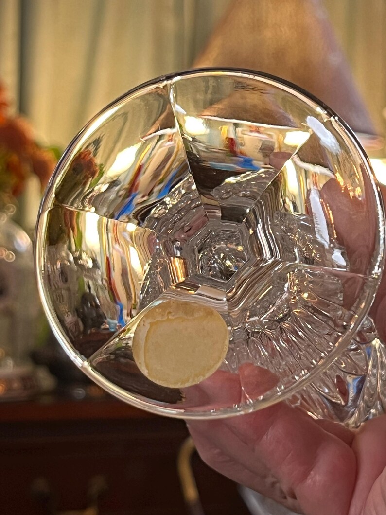 Peut inclure: Un verre en cristal clair et facett&eacute; avec une base ronde et un design g&eacute;om&eacute;trique d&eacute;taill&eacute;. Le verre a un autocollant au fond. Le verre est tenu par une personne.