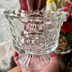 May include: A clear glass pedestal bowl with a textured, diamond-shaped pattern. The bowl has a wide, flared top and a tall, slender base.