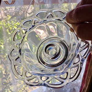 May include: A clear glass bowl with a scalloped edge and a decorative, raised, circular pattern in the center. The bowl is made of clear glass and has a delicate, feminine design.