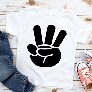 May include: White t-shirt with a black hand making the number three sign.