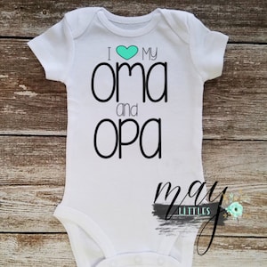 Peut inclure: Combinaison blanche pour bébé avec un texte noir qui dit "J'aime mon oma et mon opa" avec un cœur turquoise.