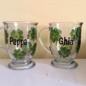 May include: Two clear glass mugs with green shamrock designs and black lettering. The mugs say "Pappa" and "Ghia".