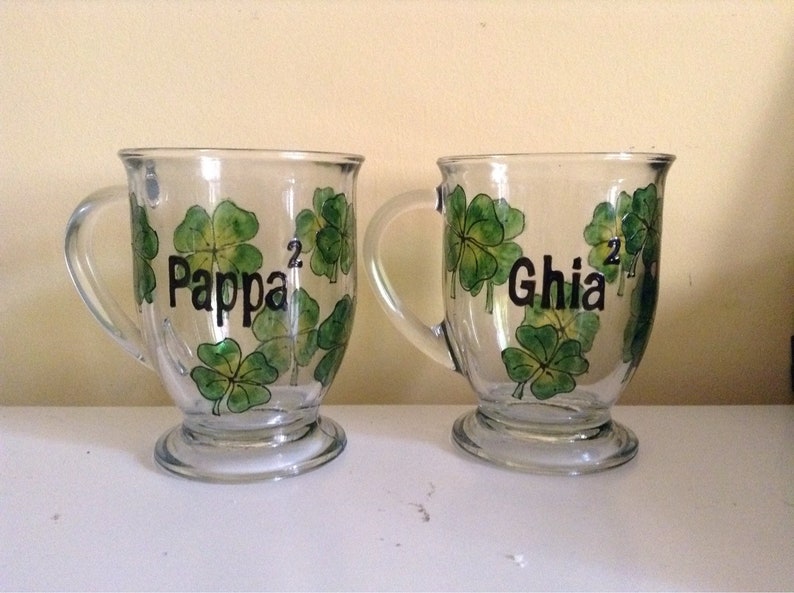 May include: Two clear glass mugs with green shamrock designs and black lettering. The mugs say "Pappa" and "Ghia".