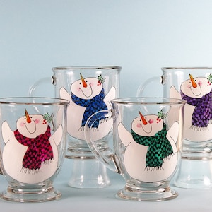 May include: Four glass mugs with snowman designs. Each mug features a snowman with a different colored scarf: blue, purple, pink, and green.
