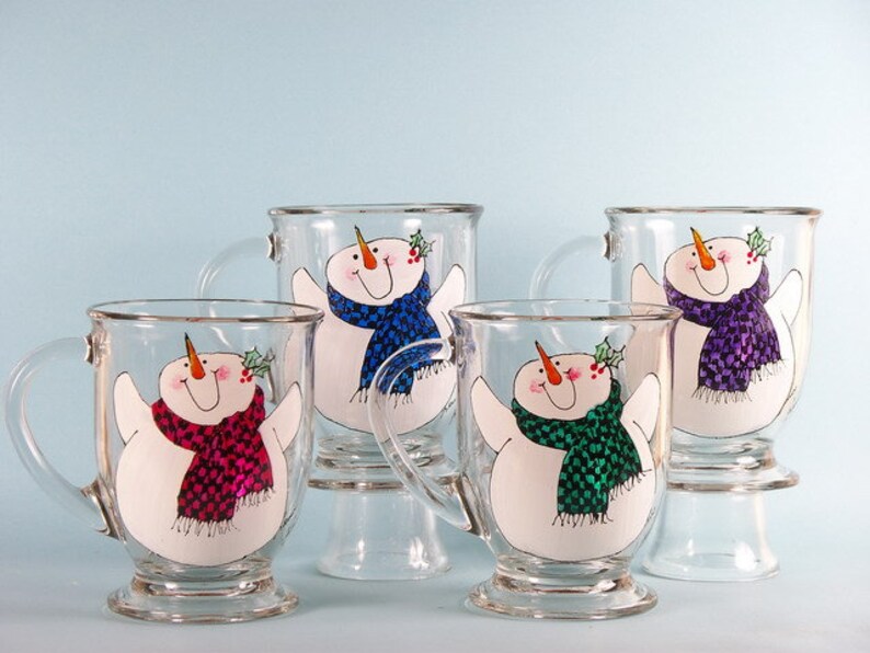 May include: Four glass mugs with snowman designs. Each mug features a snowman with a different colored scarf: blue, purple, pink, and green.