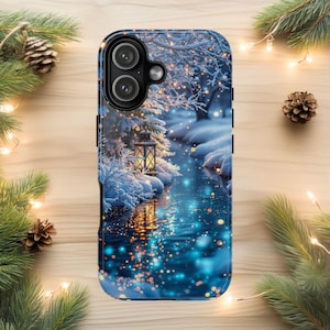 May include: A phone case featuring a winter scene with a lantern, snow-covered trees, and a flowing river. The design has a blue and white color scheme with sparkling lights, creating a festive holiday theme.