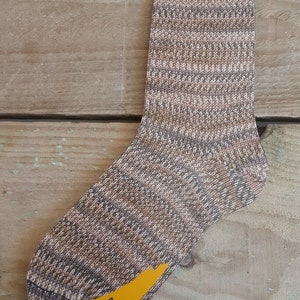 May include: A brown, beige and white patterned sock with the text "Taiga 5467 Jubilee Color" on the bottom.