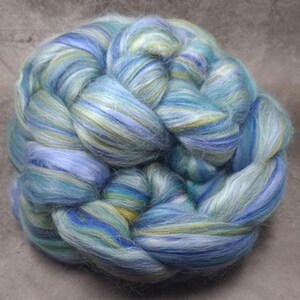 May include: A bundle of blue, green and yellow hand-spun fibre. The fibre is arranged in a braided pattern.