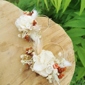 May include: A pair of gold hoop earrings with dried flowers and feathers. The flowers are white and orange, and the feathers are white and brown.