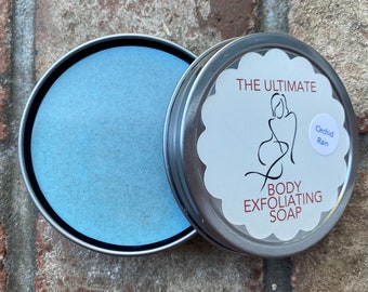 Può includere: Una scatola di latta argentata con un sapone esfoliante blu all'interno. Il coperchio della scatola ha un'etichetta bianca con il testo "The Ultimate Body Exfoliating Soap" e "Orchid Rain".