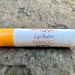 May include: A white lip balm tube with a yellow cap. The tube has the text "Lip Balm MANGO" printed on it.