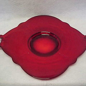 May include: A red glass serving tray with two handles. The tray has a scalloped edge and a raised center.