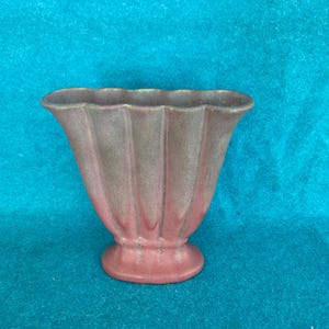 May include: A pink and green ceramic vase with a scalloped rim and a fluted design. The vase has a wide base and a narrow opening.