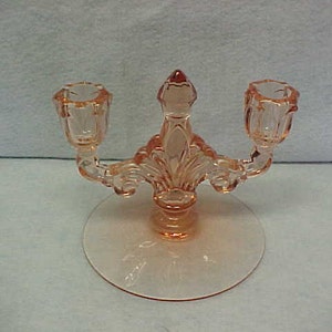 May include: A pink glass candle holder with two candle cups and a decorative base.