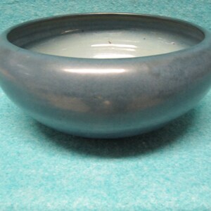 May include: A blue ceramic bowl with a smooth, glossy finish. The bowl is round and has a wide, shallow opening.