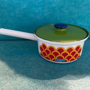 May include: White enamel saucepan with a green lid and a red, yellow, and orange geometric pattern. The saucepan has a white handle and the text "peter max" on the bottom.
