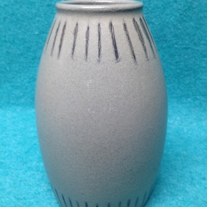May include: A light gray ceramic vase with a textured surface and black lines around the top and bottom.