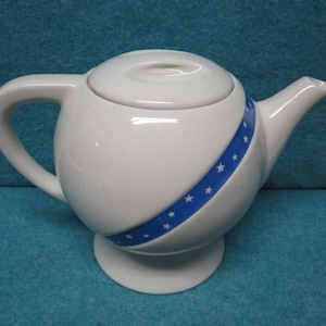 May include: White ceramic teapot with a blue and white star design. The teapot has a round body and a lid.