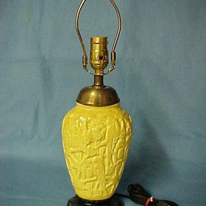 May include: A yellow ceramic table lamp with a carved design of birds and branches. The lamp has a brass base and a black cord.