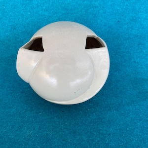 May include: A white ceramic ashtray with a unique design. The ashtray has a rounded shape with two rectangular openings and a central depression. The ashtray is set against a blue background.