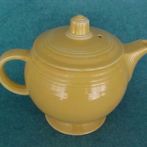 May include: A yellow ceramic teapot with a lid and a handle. The teapot has a smooth, glossy finish and a rounded body.