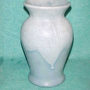 May include: A light blue ceramic vase with a textured surface. The vase has a rounded body, a flared rim, and a base. The color transitions from white to light blue, creating a unique aesthetic. This decorative vase is suitable for displaying flowers or as a standalone art piece.