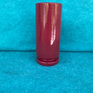 May include: A tall, cylindrical vase made of ceramic with a deep burgundy red glaze. The vase has a slightly flared rim and a rounded base.