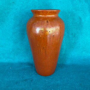 May include: A terracotta vase with a textured, speckled surface. The vase has a rounded body and a slightly flared opening.