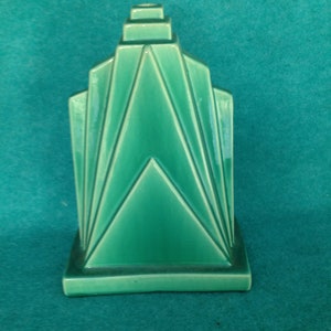May include: A green ceramic vase with a geometric design. The vase is shaped like a pyramid with a square base.