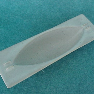 May include: A light blue ceramic ashtray with a long, narrow, oval shape and two small indentations on each end.