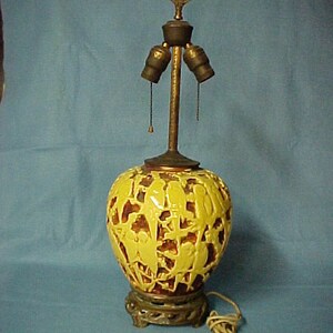 May include: A yellow ceramic lamp with a carved bird design. The lamp has a three-way socket and a gold-colored metal base.