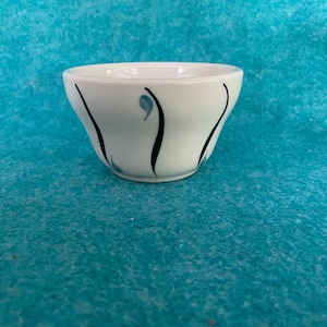 May include: A white ceramic bowl with black and blue abstract designs. The bowl is slightly flared at the top and has a rounded bottom.