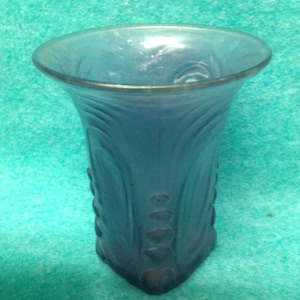 May include: A blue glass vase with a textured, wavy design. The vase has a wide mouth and a narrow base.