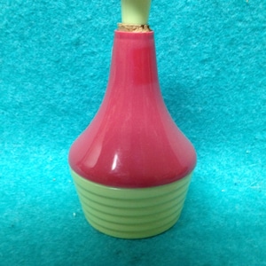 May include: A pink and green plastic bottle with a ribbed design and a small, pink, round top.