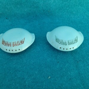 May include: Two small, light blue ceramic salt shakers with the words "Flying Saucer" printed on them.