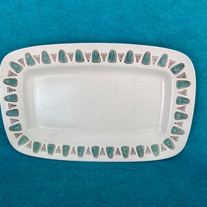May include: A white rectangular serving dish with a green and brown geometric pattern around the edge.