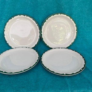 May include: Four white ceramic dinner plates with a green and white leafy design around the rim.