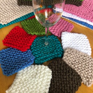 May include: A collection of colorful knitted coasters in various colors, including red, blue, green, white, brown, and teal. The coasters are arranged in a circle around a clear glass wine glass.