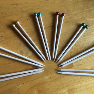 May include: A set of 10 pairs of wooden knitting needles with colourful metal tips. The needles are arranged in a fan shape on a wooden surface.