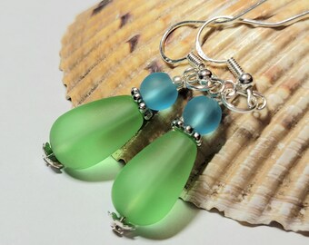 May include: A pair of dangle earrings with green and blue glass beads. The earrings have silver hooks and are accented with silver beads.