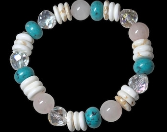 May include: A beaded bracelet featuring a variety of colorful beads. The bracelet includes turquoise, clear crystal, white, and pink beads. The beads are strung together to form a circular shape. The bracelet is set against a black background.