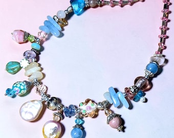 May include: A colorful necklace featuring a variety of beads and charms. The necklace includes blue, pink, and clear beads, along with unique charms. The design incorporates a mix of shapes and textures, creating a whimsical and eye-catching accessory.