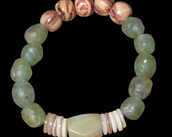 May include: A beaded bracelet featuring a mix of natural materials. The bracelet includes light green, rounded beads, brown and tan striped beads, and white shell-like beads. A light green, rectangular bead is centered.