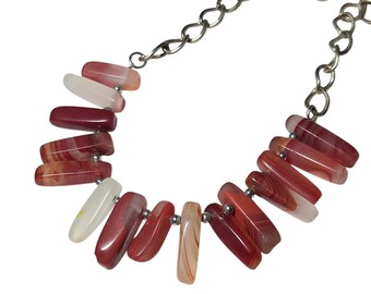 May include: A necklace featuring a silver chain and a series of rectangular, polished agate beads in shades of red, white, and orange. The beads are strung together with small silver connectors, creating a unique and eye-catching design.