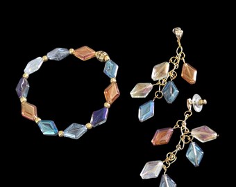 May include: A bracelet and earrings set featuring iridescent, diamond-shaped beads in shades of blue, orange, and purple. The bracelet has gold-colored accents, and the earrings dangle from gold-colored chains.
