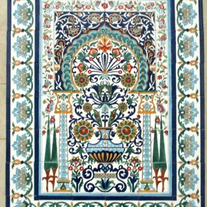 Op de afbeelding: Een decoratieve tegel met een blauw, groen en wit bloemenpatroon. De tegel heeft een centrale vaas met een bloemenontwerp en twee hoge, slanke kolommen aan weerszijden. De tegel is omgeven door een rand van blauwe, groene en witte bloemenontwerpen.