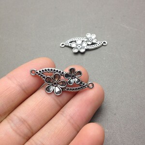 May include: Two silver-toned metal flower charms with a decorative design. Each charm has two loops for attaching to jewelry or other crafts.