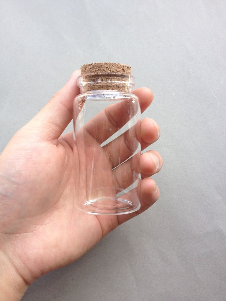 May include: A clear glass bottle with a cork stopper. The bottle is empty and has a cylindrical shape.